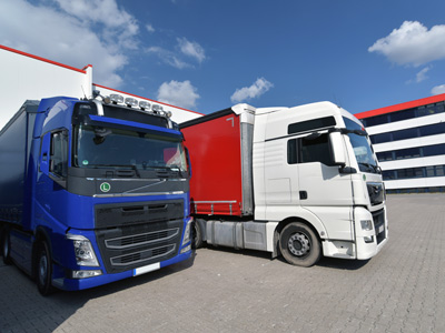 Zwei Lkw in einem Lagerbereich, ein blauer und ein weißer.